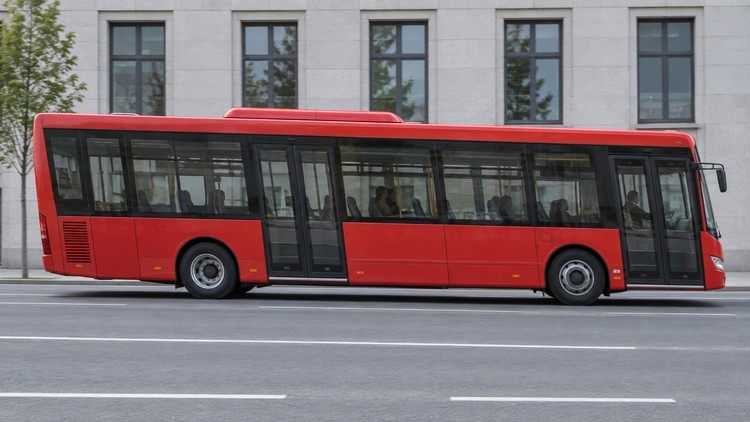 Красный автобус с наклонёнными стойками кузова на фоне здания